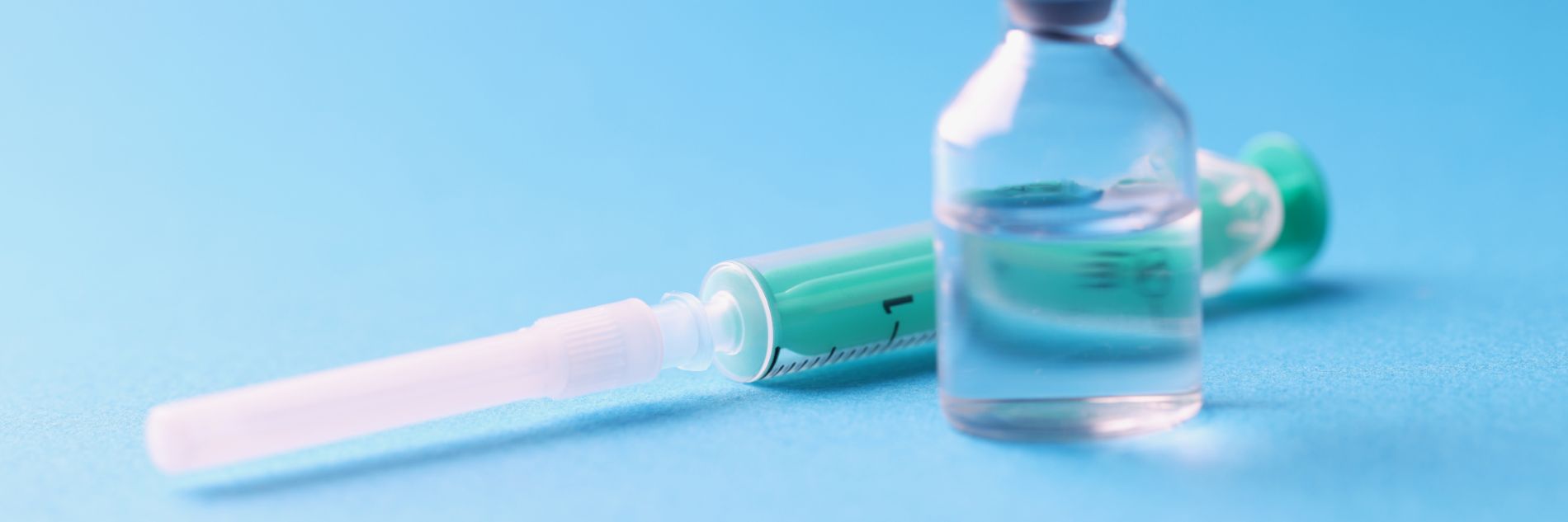 Primer plano de un frasco de vidrio con medicina y jeringa estéril sobre fondo azul
